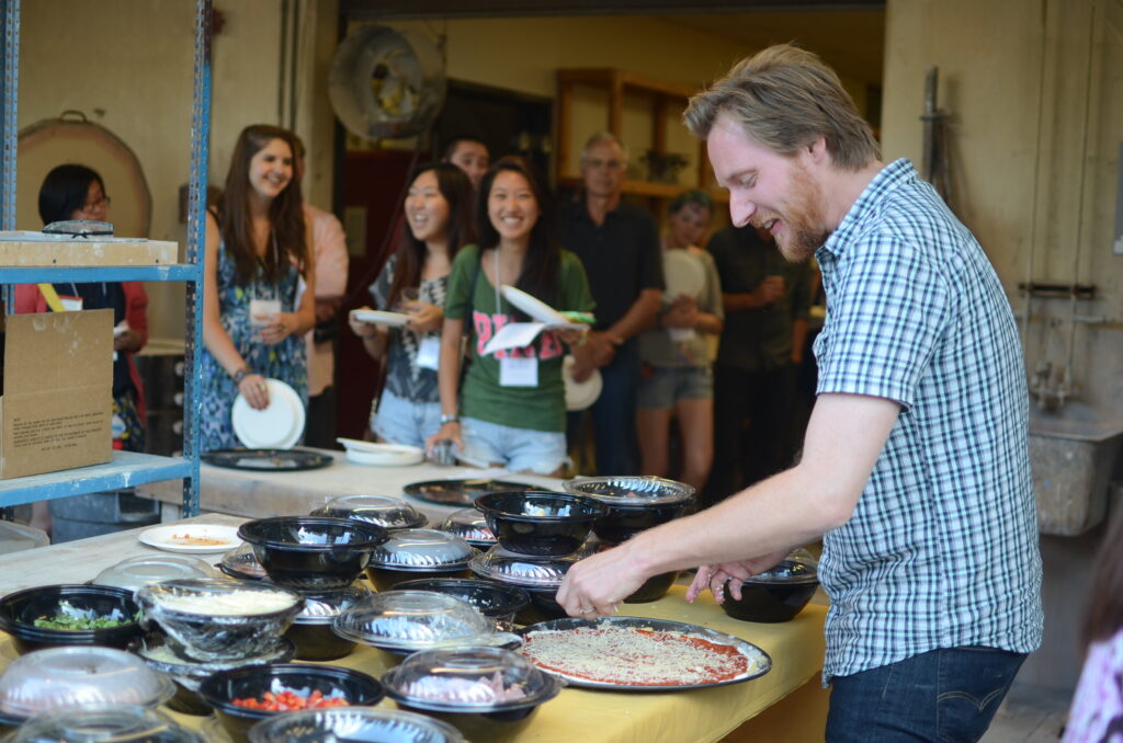 Man making pizza while group of people wait with plates.