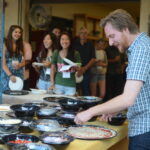 Man making pizza while group of people wait with plates.