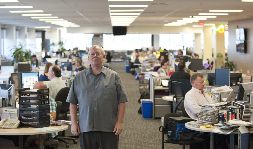 Man standing in office as people work.