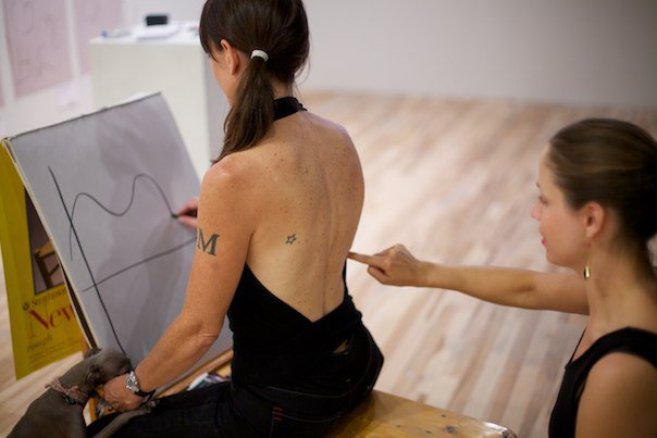 Woman tracing back of woman drawing on pad.