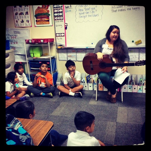 teacher with guitar sitting with young students