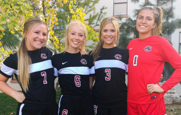 Four women soccer players posing and smiling for a photo in their Chapman team uniforms.