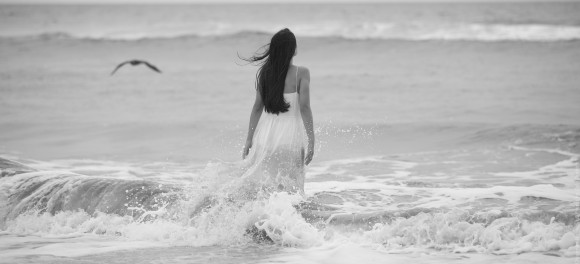 Woman in long white dress walking into the ocean.