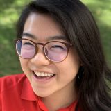 Young woman with dark hair and glasses smiling.