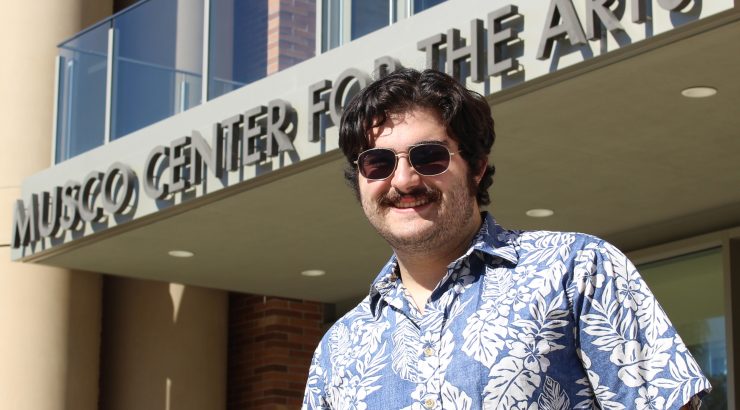 Young man with short dark hair, mustache and sunglasses standing in front of Musco Center.