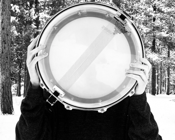 person holding snare drum in front of their face with snow and trees in background