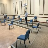 Large room with people moving chairs far apart.