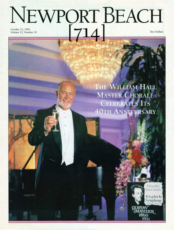 Cover of Newport Beach magazine featuring William Hall dressed in a tuxedo holding a glass of champagne under a crystal chandelier with a piano in the background.