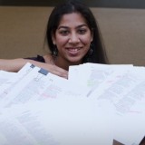 Woman posing with many marked up pages of writing.