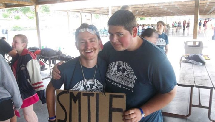 Image of two men holding a sign that reads SMILE