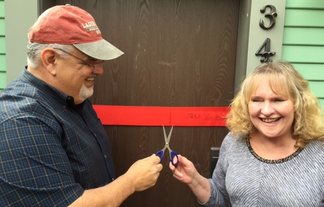 Man and woman cut ribbon in front of door.