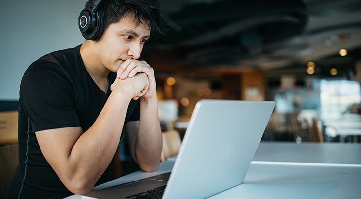 Young man looking at a laptop wearing headphones