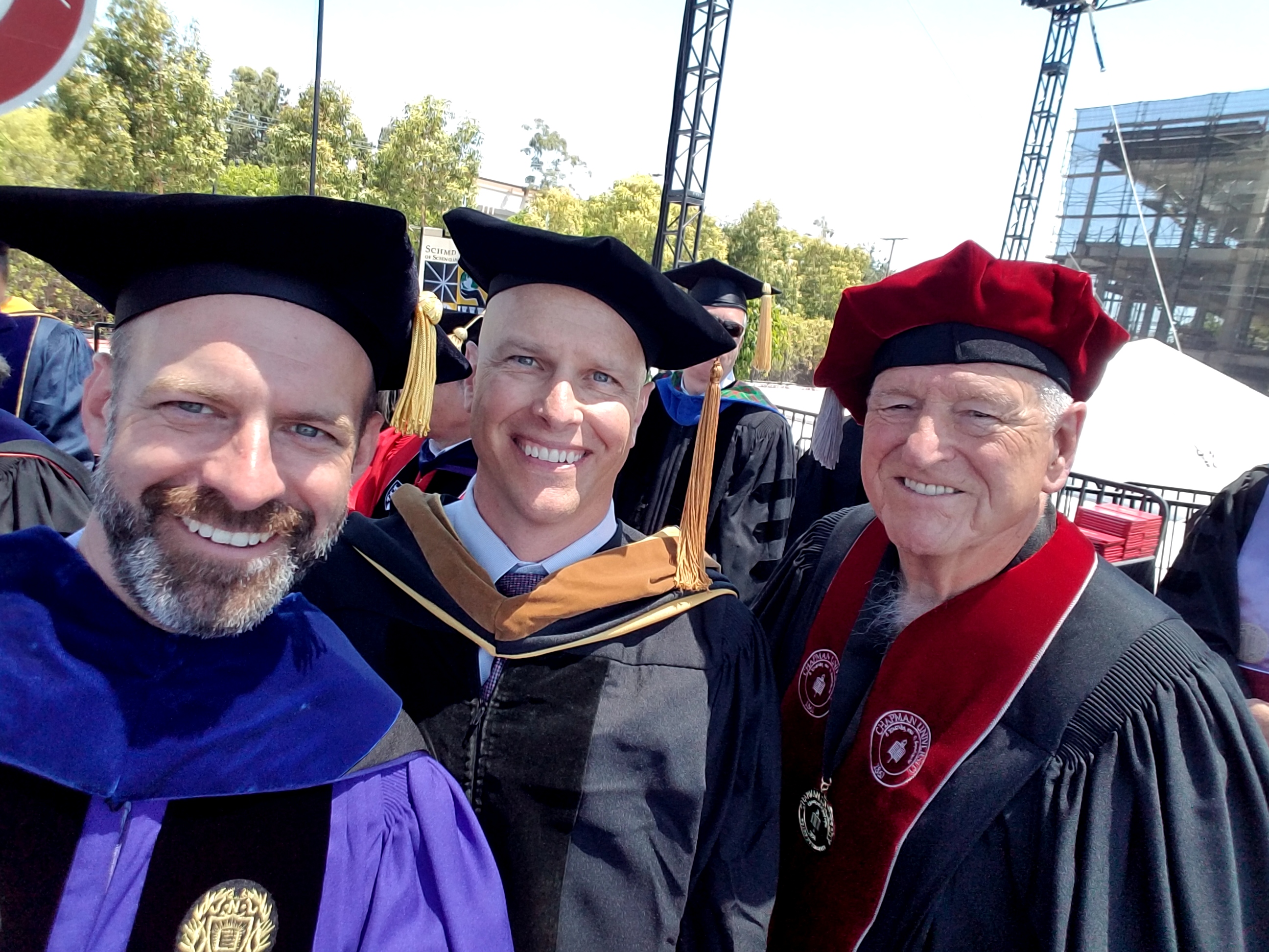 Schmid College Dean Andrew Lyon (left) on stage at 2017 Commnecement ceremony with keynote speaker Paul Cook (center) and Trustee Richard Schmid (right)