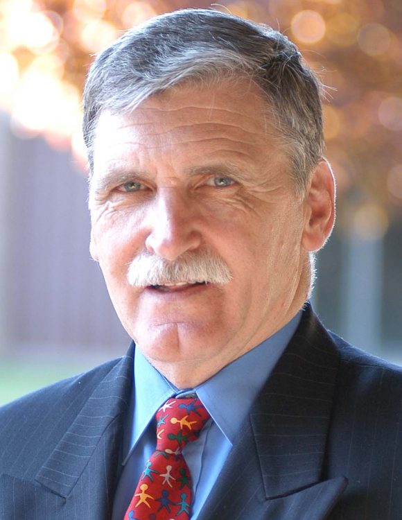 Headshot of Romeo Dallaire wearing a dark suit and red tie with shapes of people of various colors holding hands