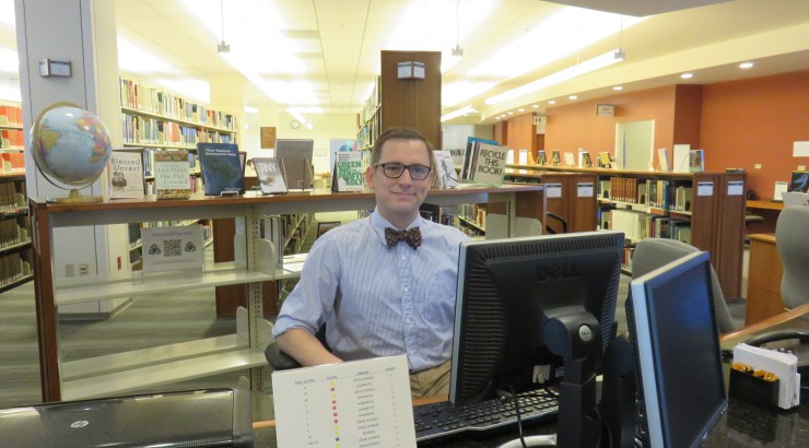 Man in bowtie using computer in library.