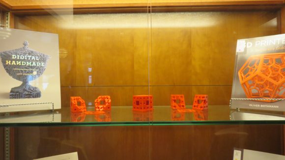 A shelf in a display case with two books on either side, and three small orange objects between the books