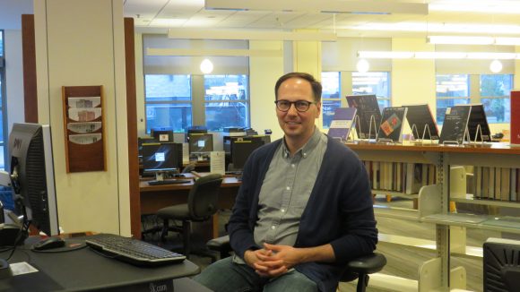 Male librarian sits at reference desk