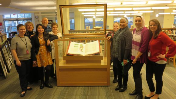 Group of faculty and staff stand around an open case with illustrated bible inside.