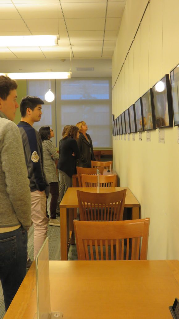 Group of students stand, looking at art hanging on the wall.