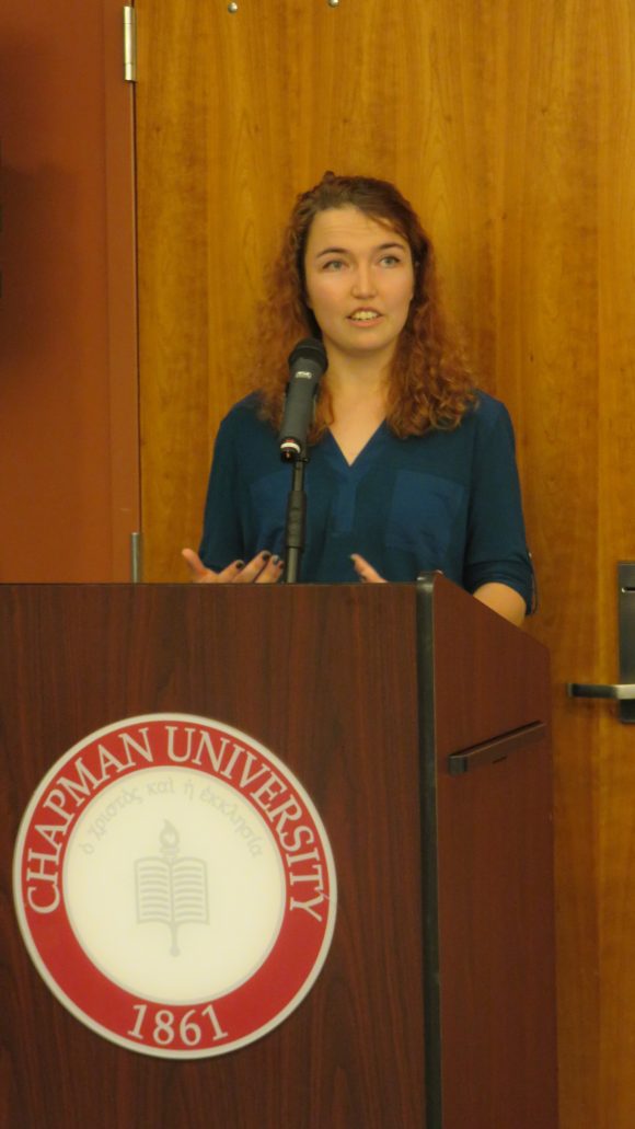Young woman stands behind a podium talking.
