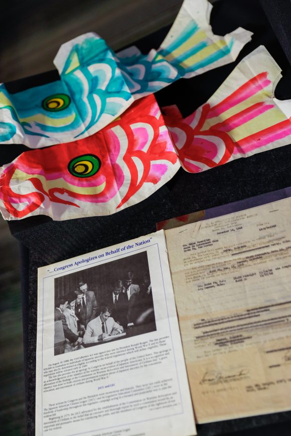 Two colorful paper kites decorated like fish sit on a table behind two archival documents.