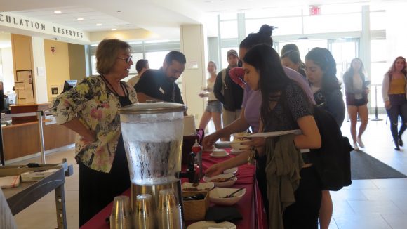 A woman and man stand on the left side of the photo, behind a table with water and ice cream on it. On the right, a long line of students get their ice cream.