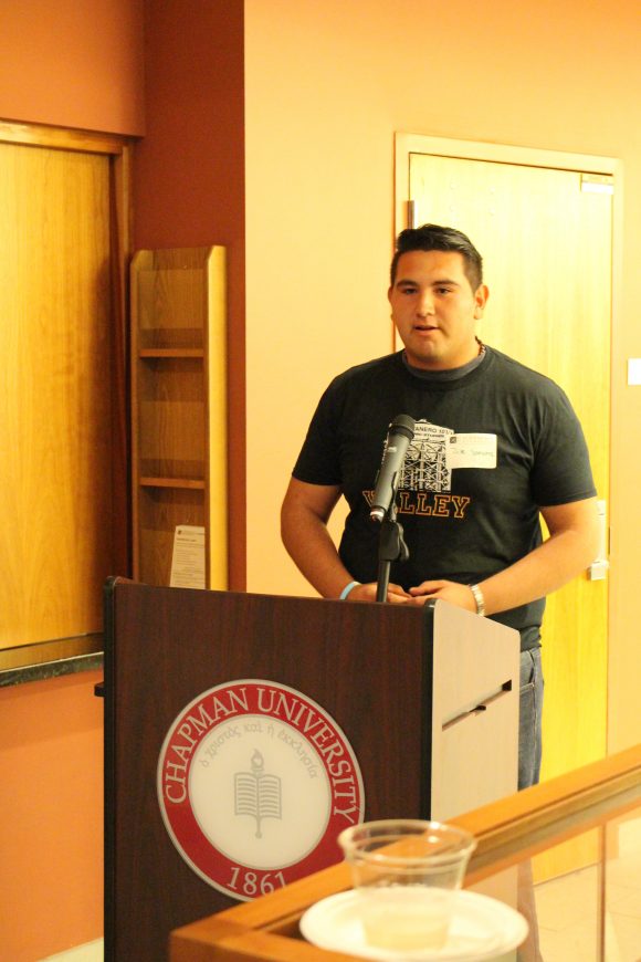 A young man in a t-shirt stands behind a microphone at a podium.