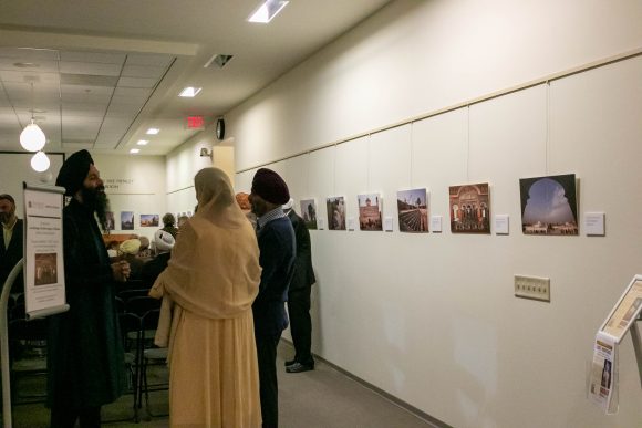 Guests with their backs turned to the camera stand next to photos displayed on the wall to the right of the frame