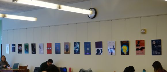 Book covers, printed as 11" x 17" posters, hanging on the wall above studying students.
