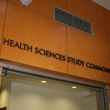 Photograph of the outside of the Health Sciences Study Commons, showing those words on a wooden wall over an open door