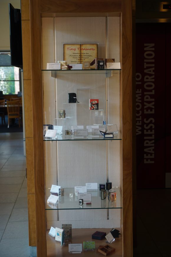 A tall narrow display case containing several miniature books.