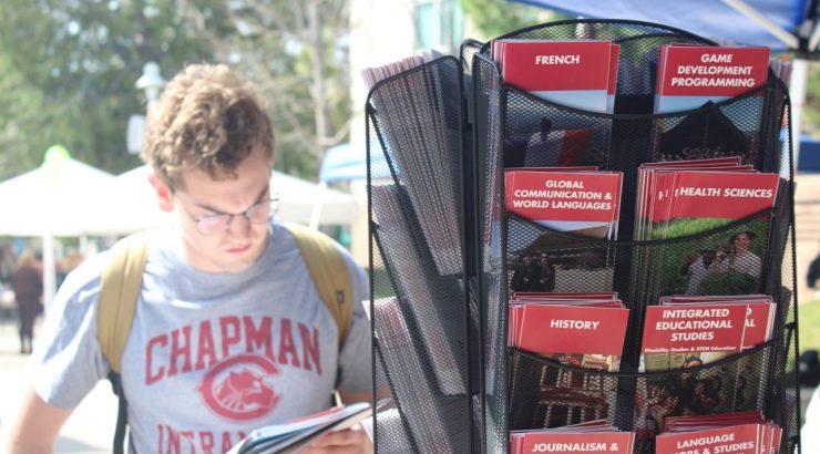 Student reading brochure, standing next to mobile shelf of other brochures with majors listed at study abroad fair.