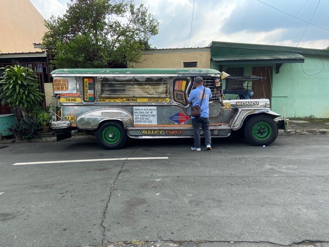 A man taking care of his Jeepney truck. The truck is long and maybe about 8 feet tall.