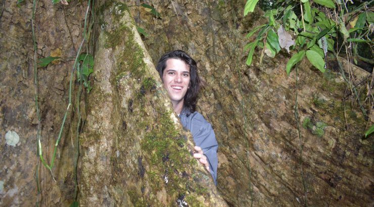 Student behind large tree trunk